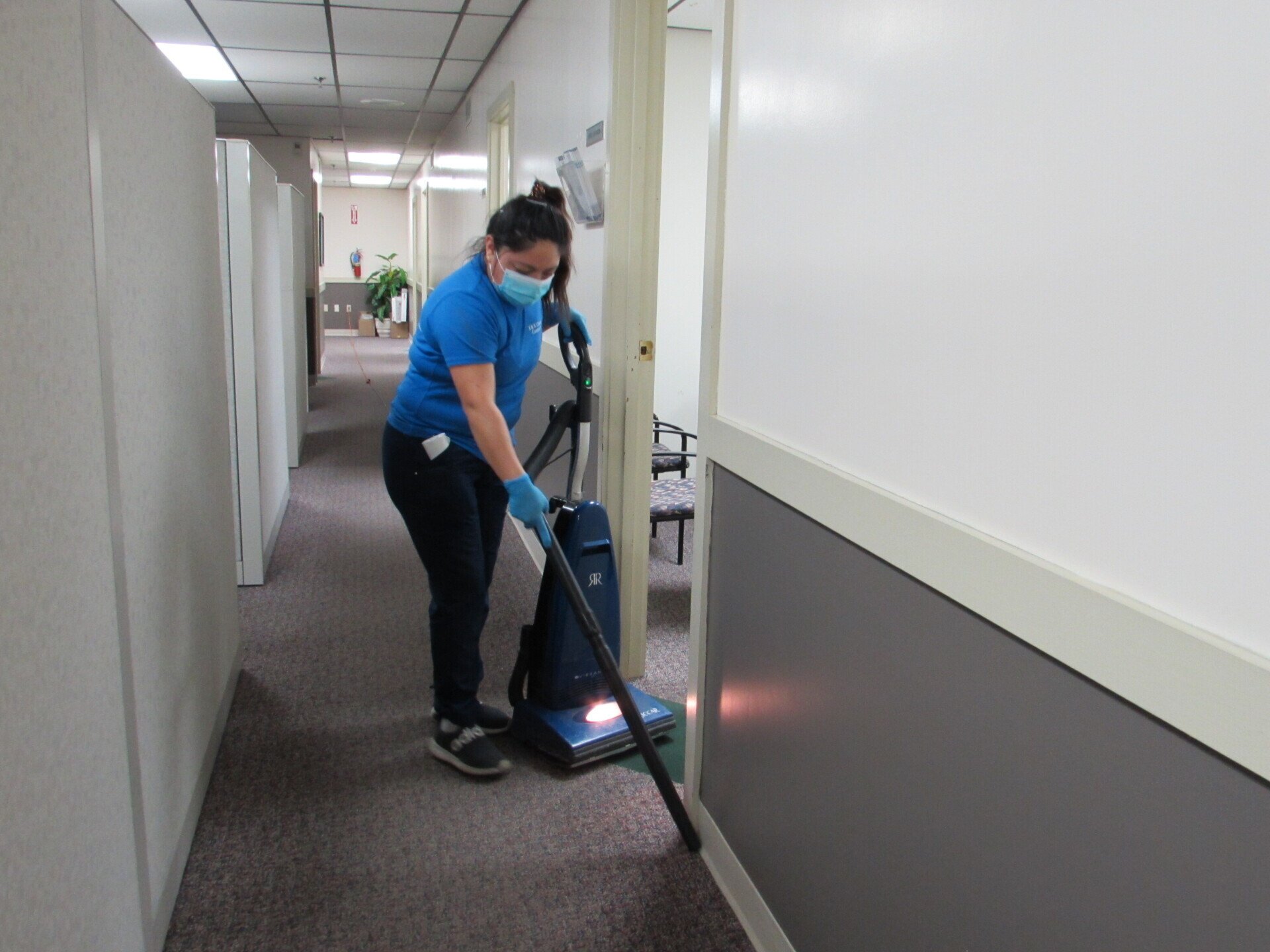 Woman wearing a mask vacuuming a commercial office hallway.